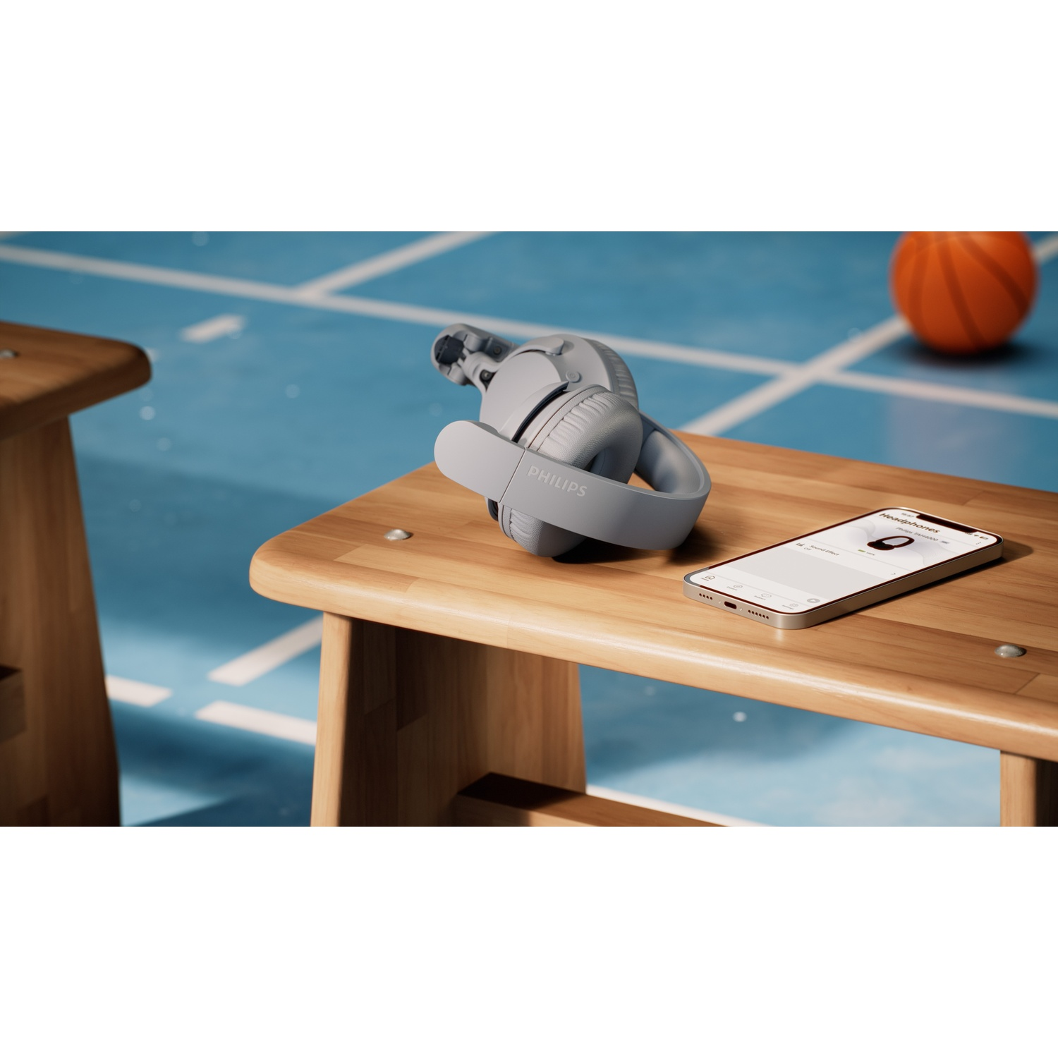 Cuffie grigie e smartphone su una panchina di legno. Pallone da basket sullo sfondo.