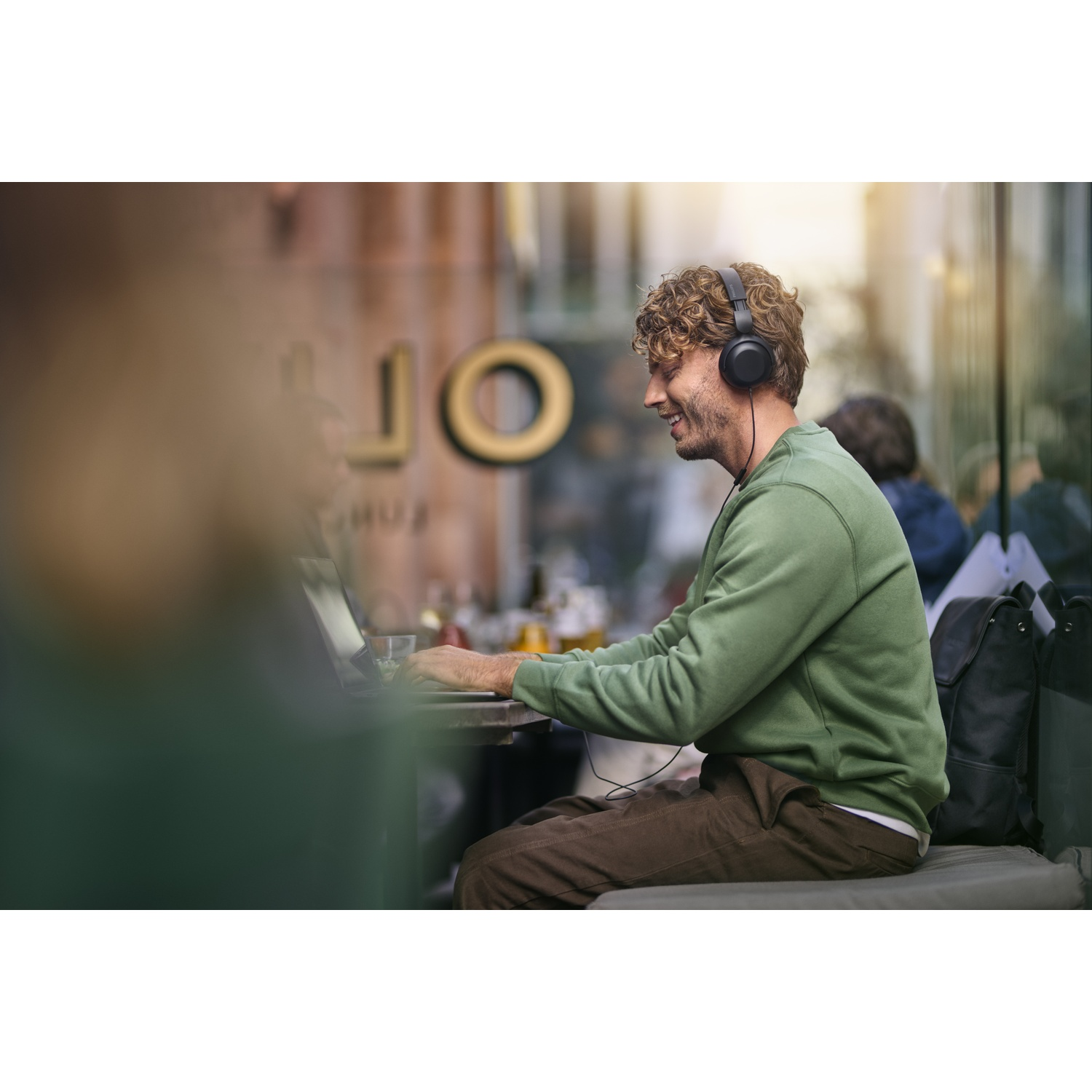 Uomo con cuffie lavora al laptop in un caffè all'aperto.