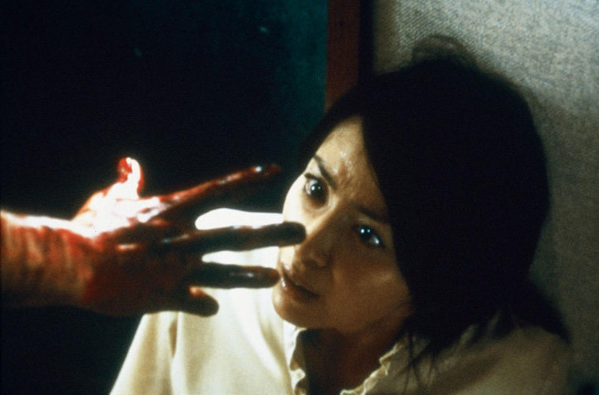 Eine blutige Hand nähert sich dem Gesicht einer Frau mit weit aufgerissenen Augen.