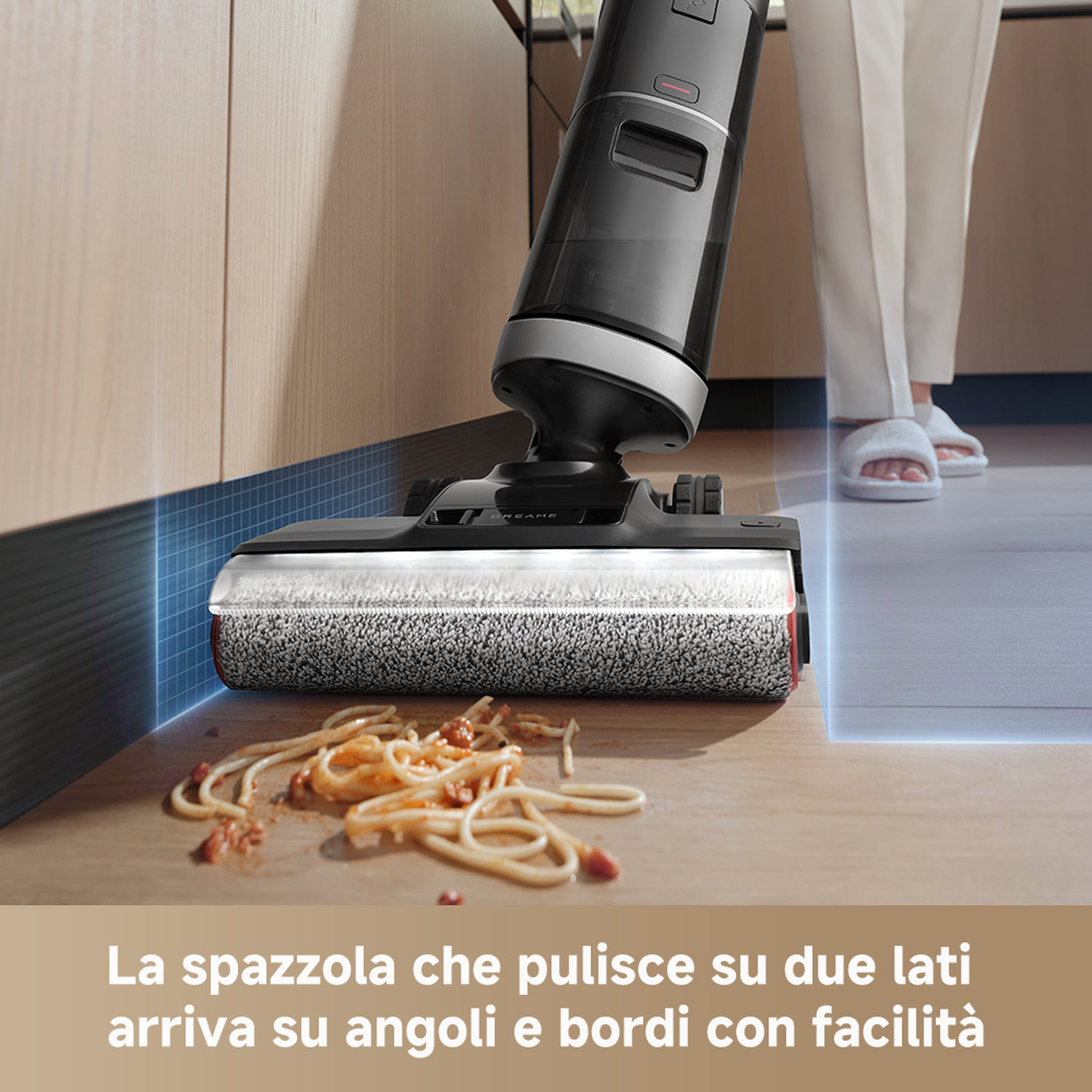 Un aspirapolvere pulisce la pasta dal pavimento, con una persona in ciabatte nelle vicinanze.