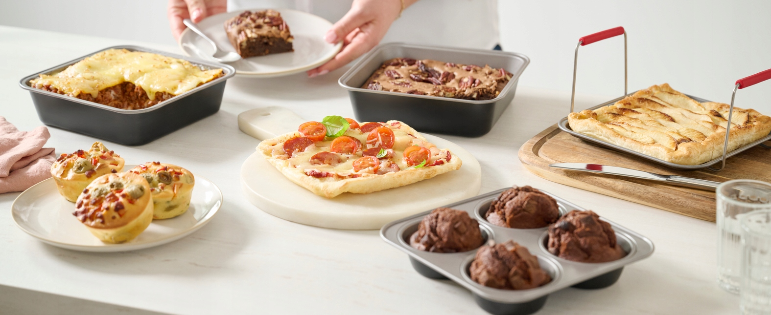 Różne wypieki na blacie kuchennym: lasagne, brownie, pizza, muffiny, szarlotka.
