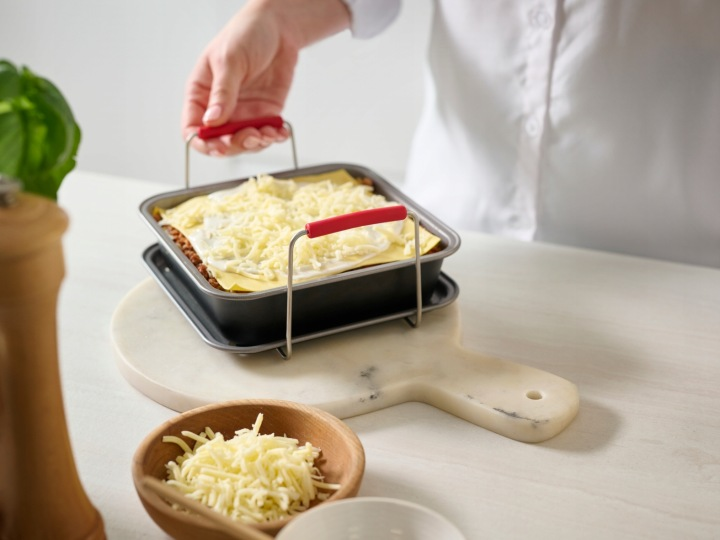 Osoba trzyma naczynie do zapiekania z lasagne i serem, gotowe do pieczenia.