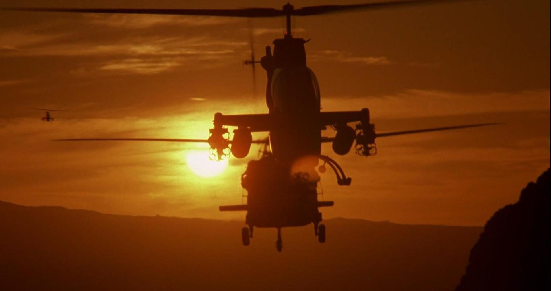 Helikopter im Gegenlicht der Sonne mit Gebirgszug im Hintergrund.
