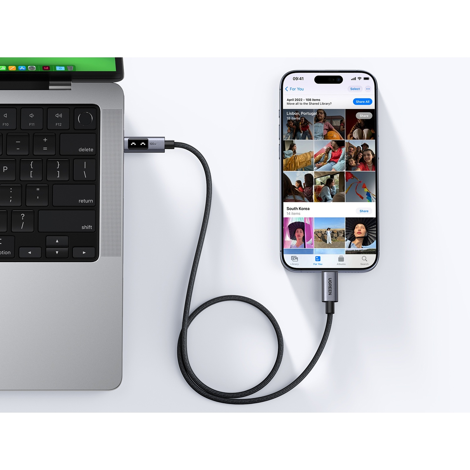 Un cavo collega un laptop a uno smartphone che visualizza foto.