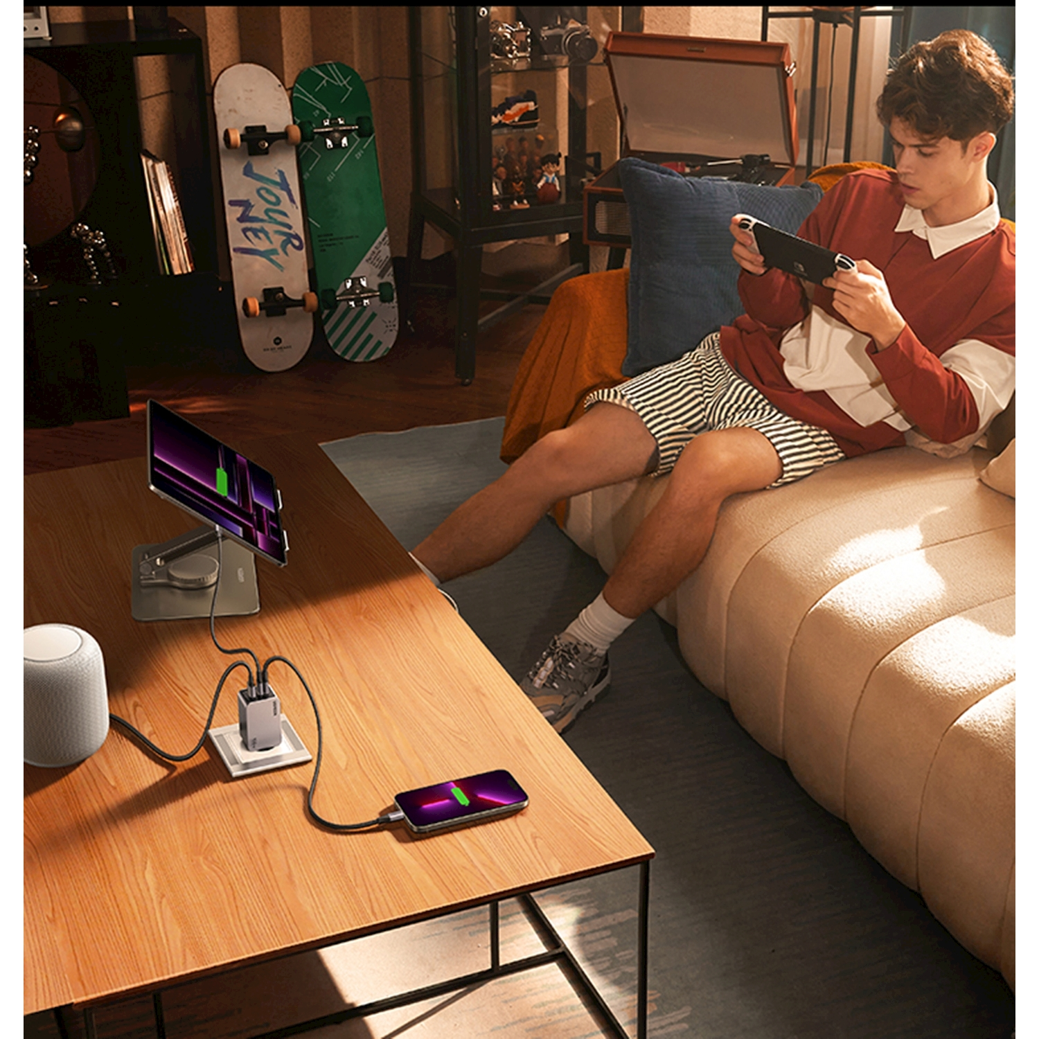 Uomo gioca a Nintendo Switch sul divano; telefono, tablet, speaker in carica.