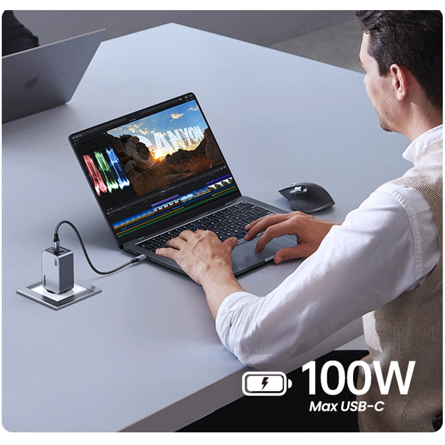 Uomo modifica video su laptop caricato da caricatore USB-C da 100W.