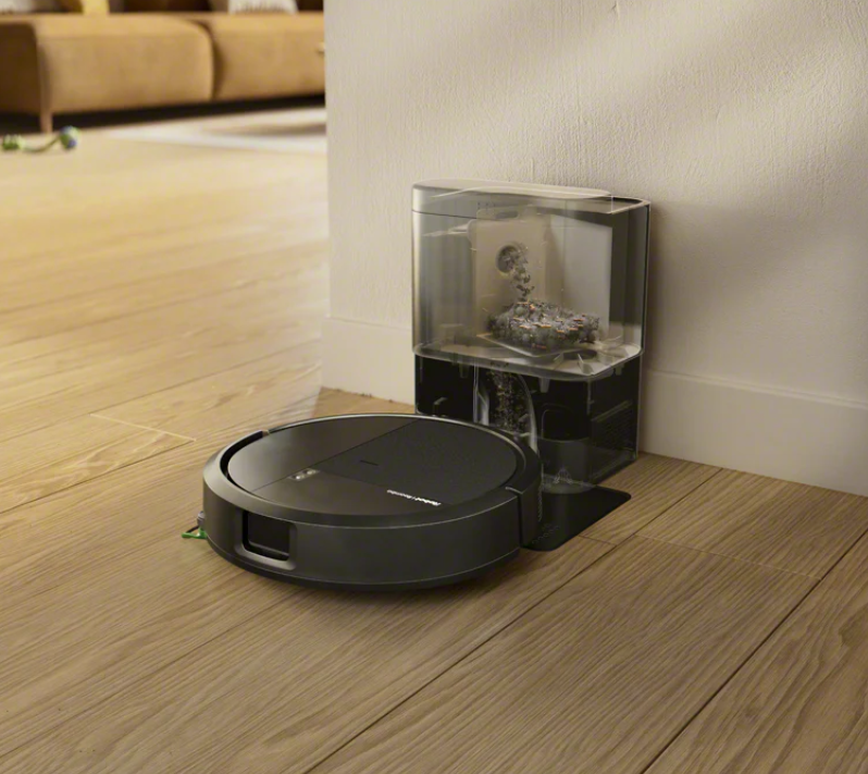 Czarny robot sprzątający stoi obok stacji ładującej z pełnym pojemnikiem na kurz.