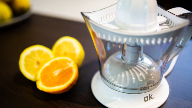 Un presse-agrumes blanc avec des citrons et une demi-orange à côté.