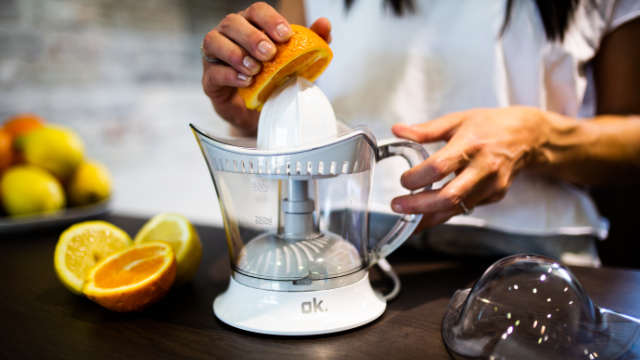 Une main presse un demi-orange sur un presse-agrumes. Des citrons sont à proximité.