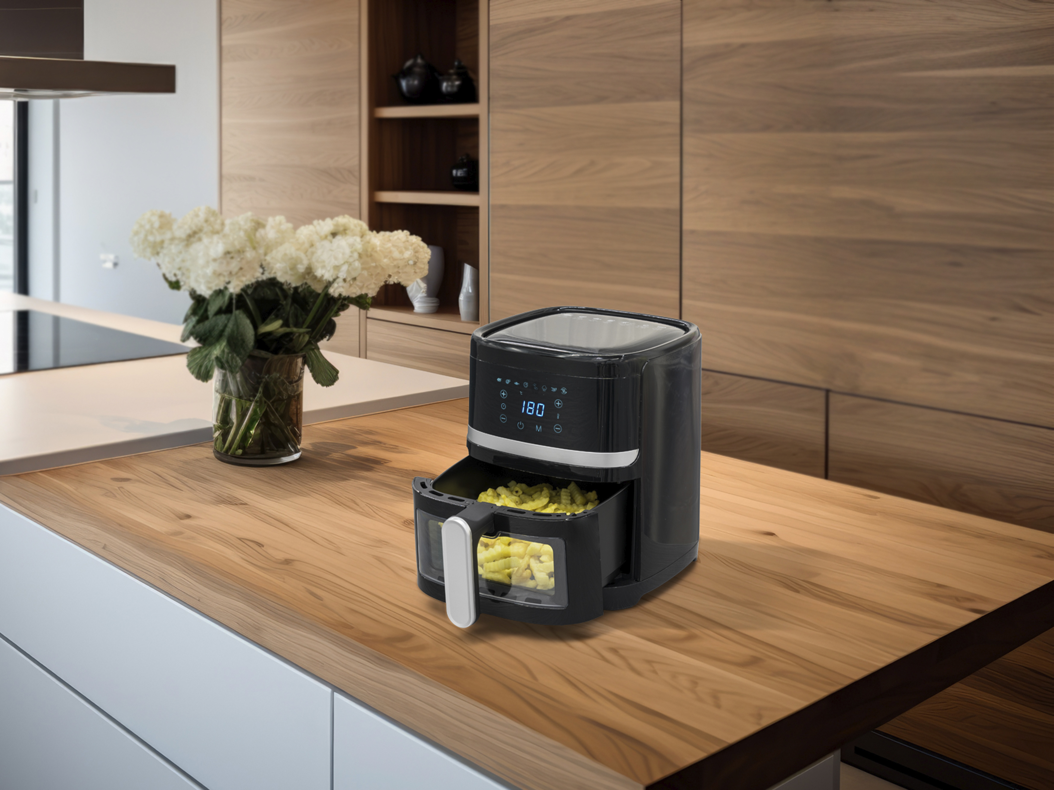 Friteuse à air noire avec frites sur surface en bois, à côté de fleurs.
