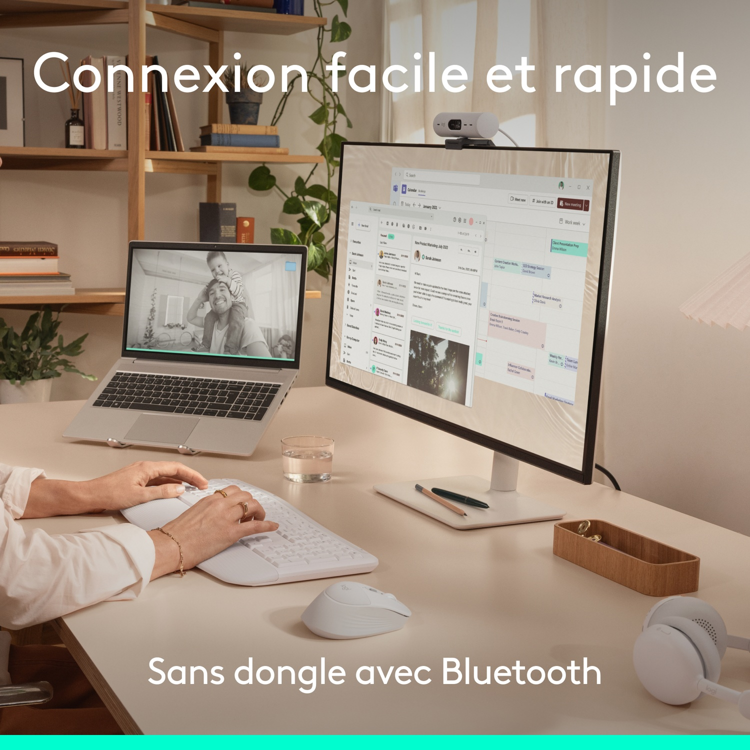 Un bureau avec ordinateur portable, écran et clavier. Une personne tape.