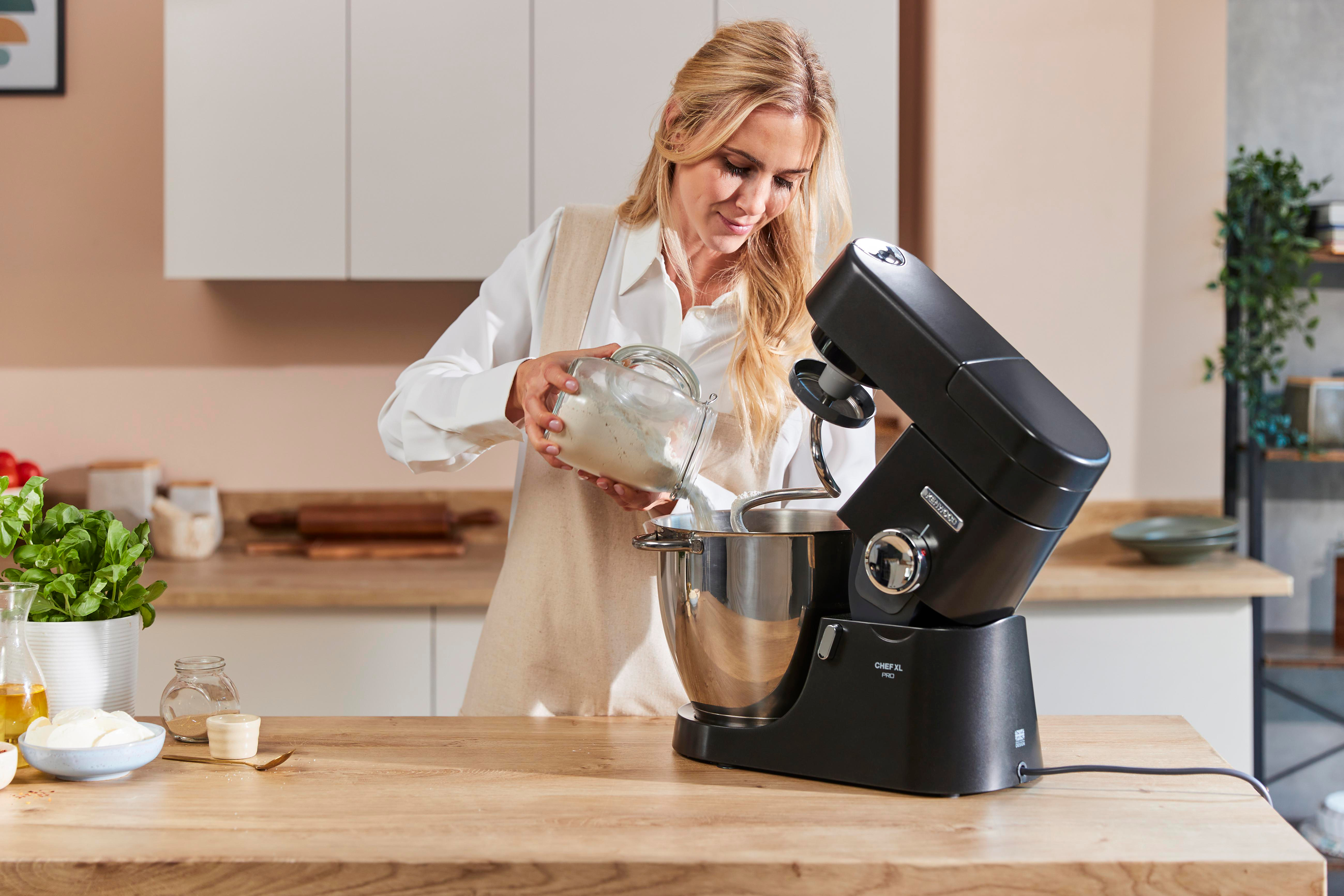 Eine Frau gibt Mehl aus einem Glas in eine Küchenmaschine.