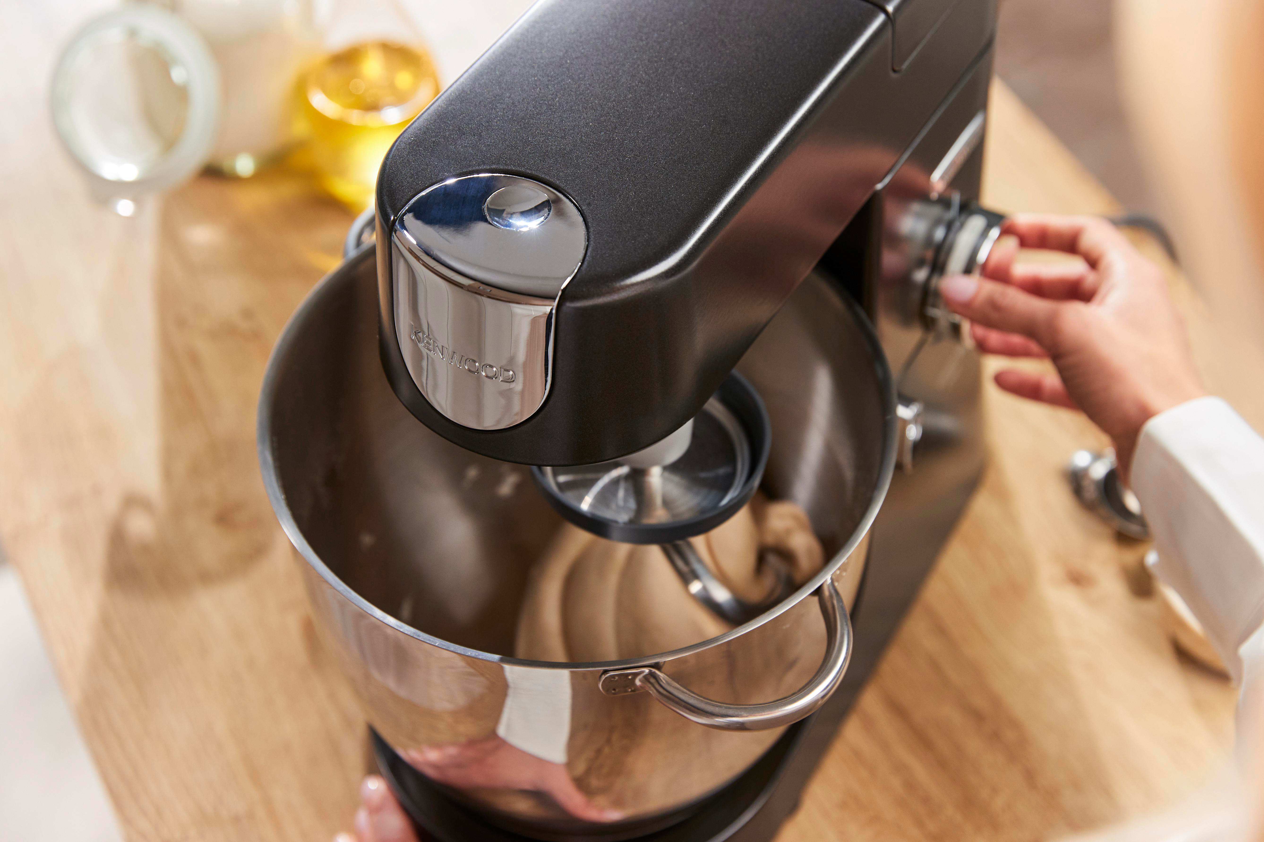 Eine Hand stellt einen schwarzen Kenwood Küchenmixer ein, der Teig in einer Edelstahlschüssel mischt.