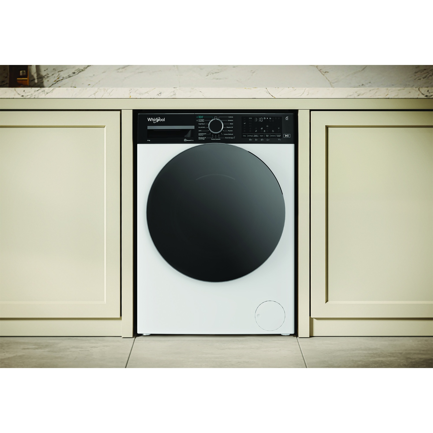 Una lavatrice Whirlpool bianca con oblò nero installata tra mobili color crema.