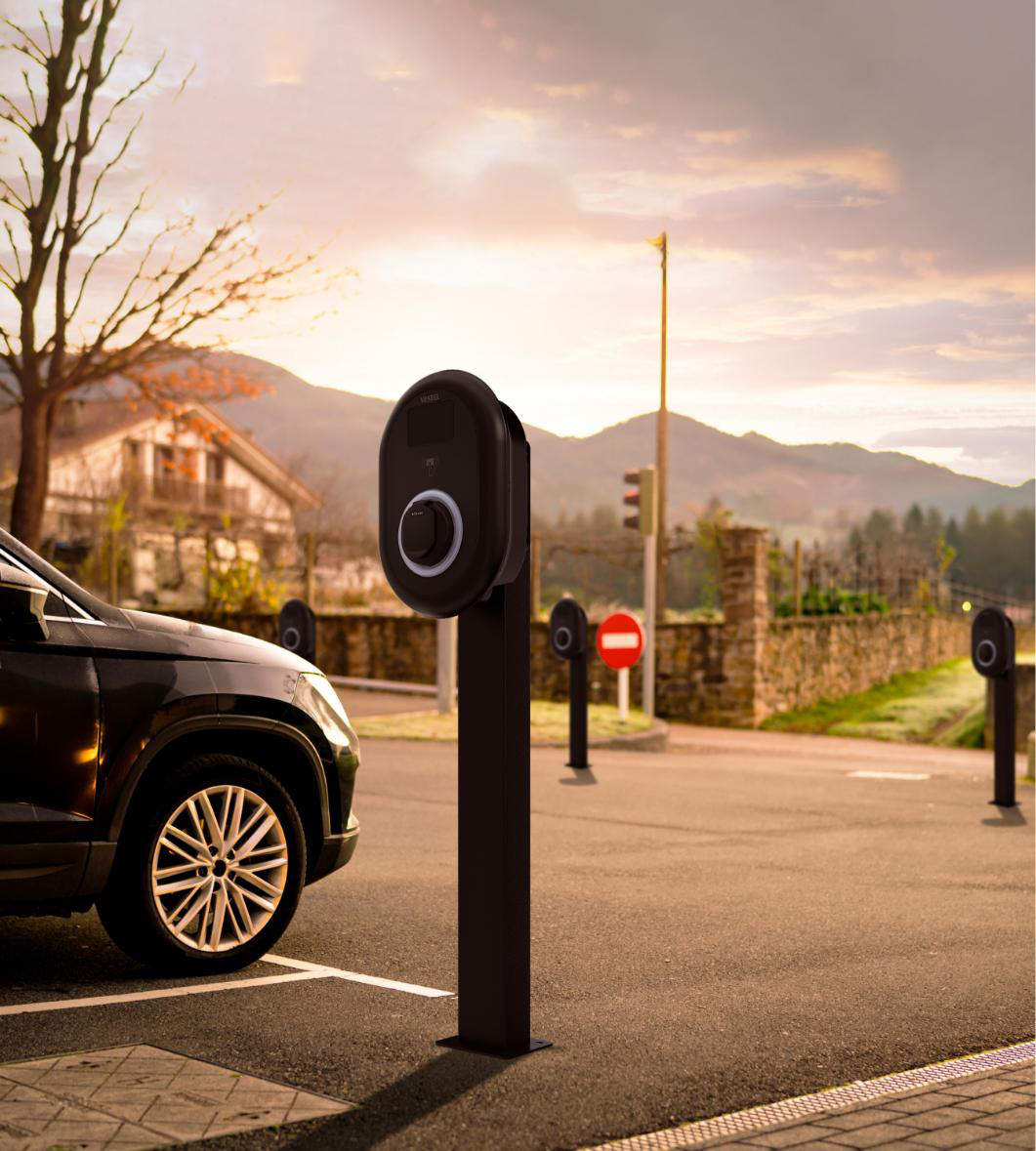 Ein dunkles Elektroauto parkt neben Ladestationen im Freien bei Sonnenuntergang.