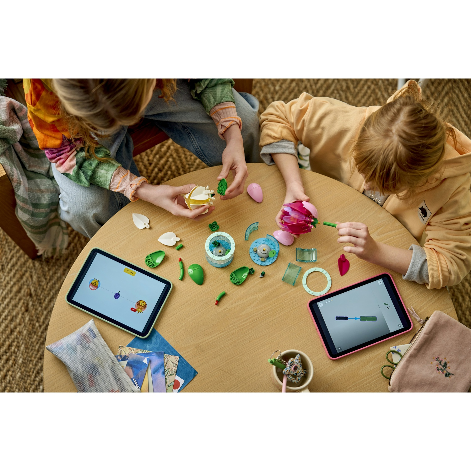 Due bambini costruiscono con i LEGO su un tavolo. Tablet mostrano istruzioni.