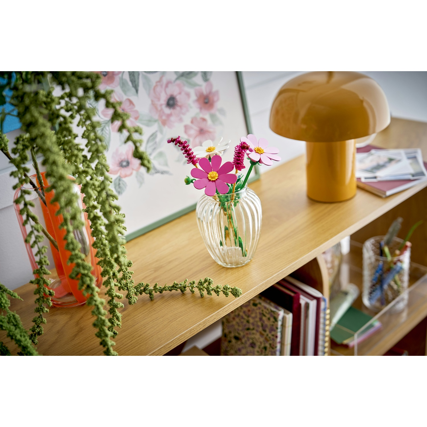 Fiori colorati in un vaso su uno scaffale, accanto a una lampada e libri.