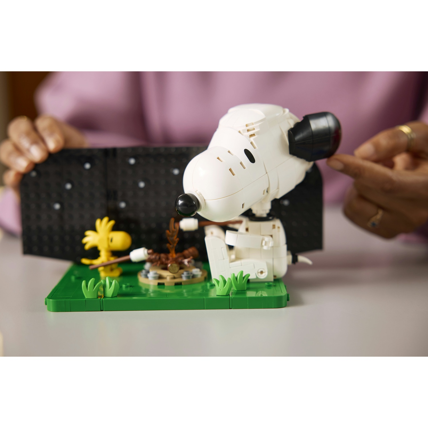 Una figura Lego bianca di Snoopy è seduta vicino a un falò con la figura di Woodstock.