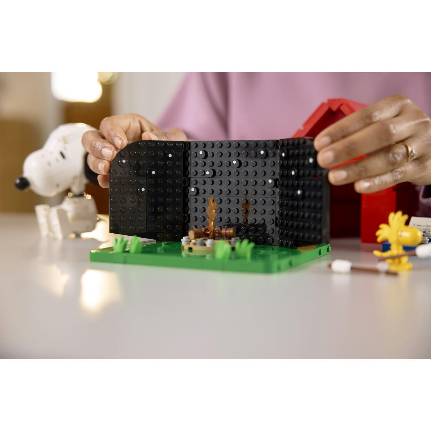 Persona che costruisce scena LEGO con Snoopy, Woodstock e falò.