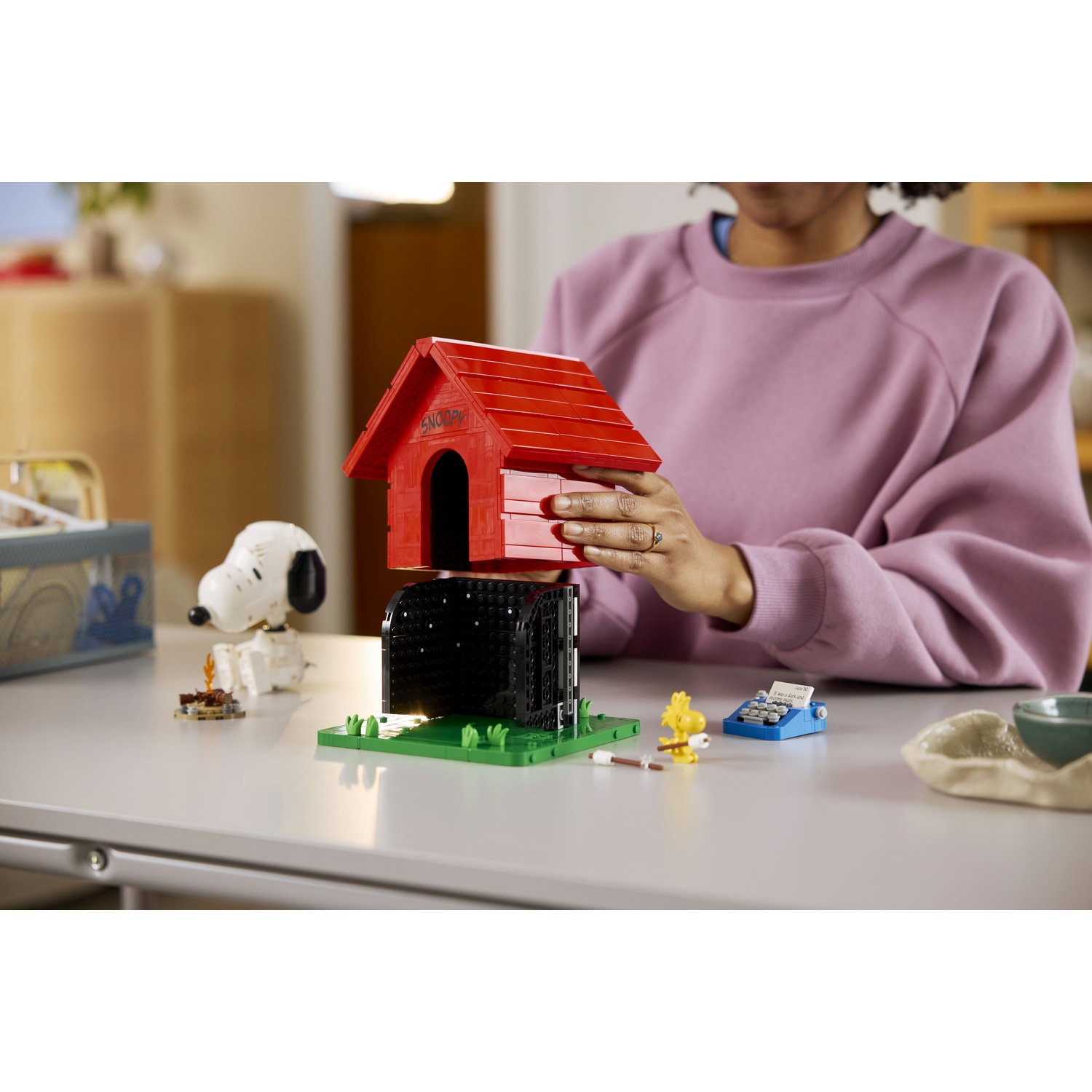 Donna assembla cuccia rossa Lego di Snoopy. Woodstock e macchina da scrivere vicini.