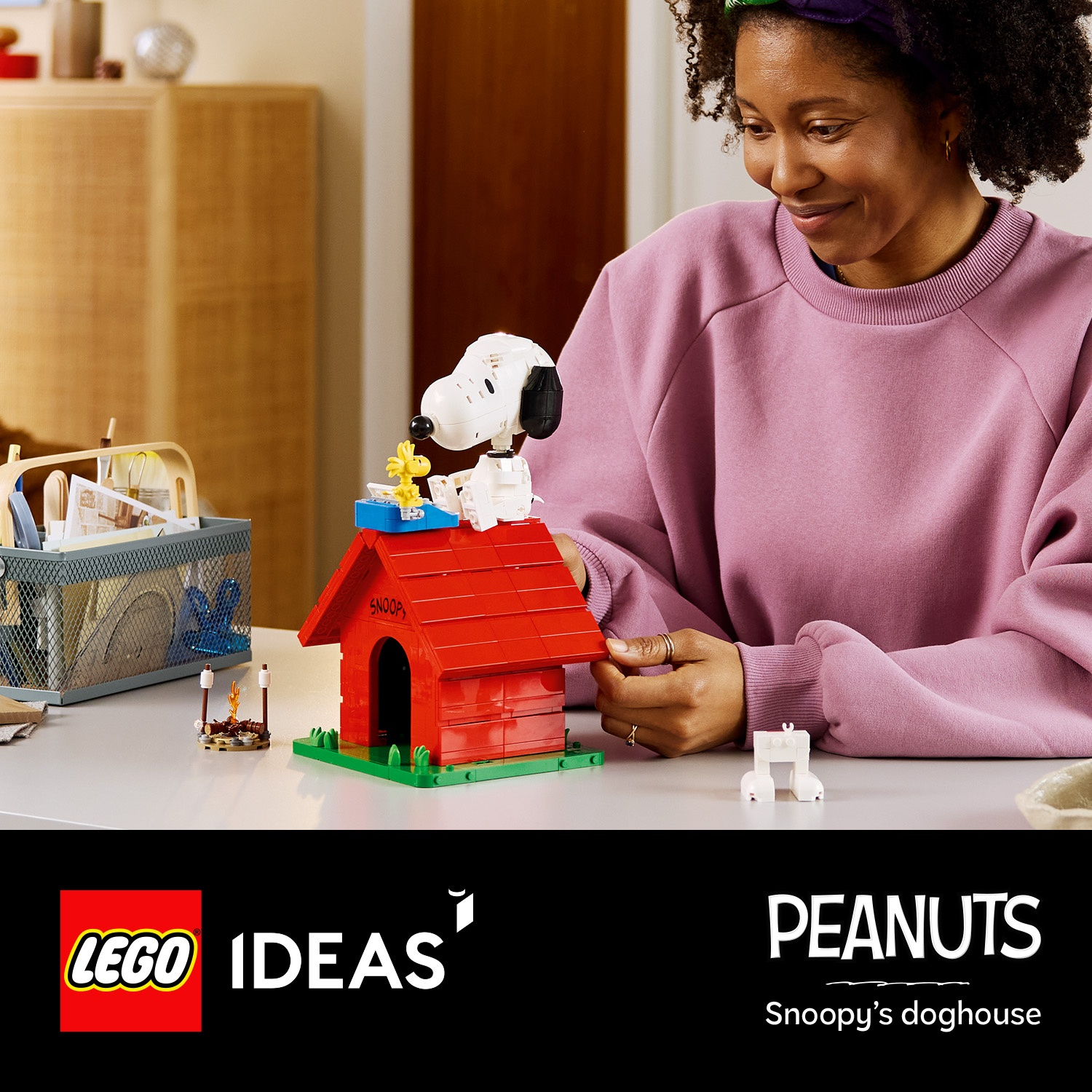 Una donna costruisce una cuccia Lego di Snoopy. Snoopy è seduto sul tetto.