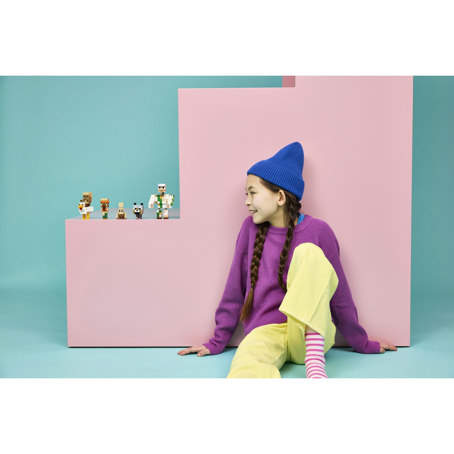 Una ragazza con maglione viola e pantaloni gialli seduta vicino a figure di Minecraft.