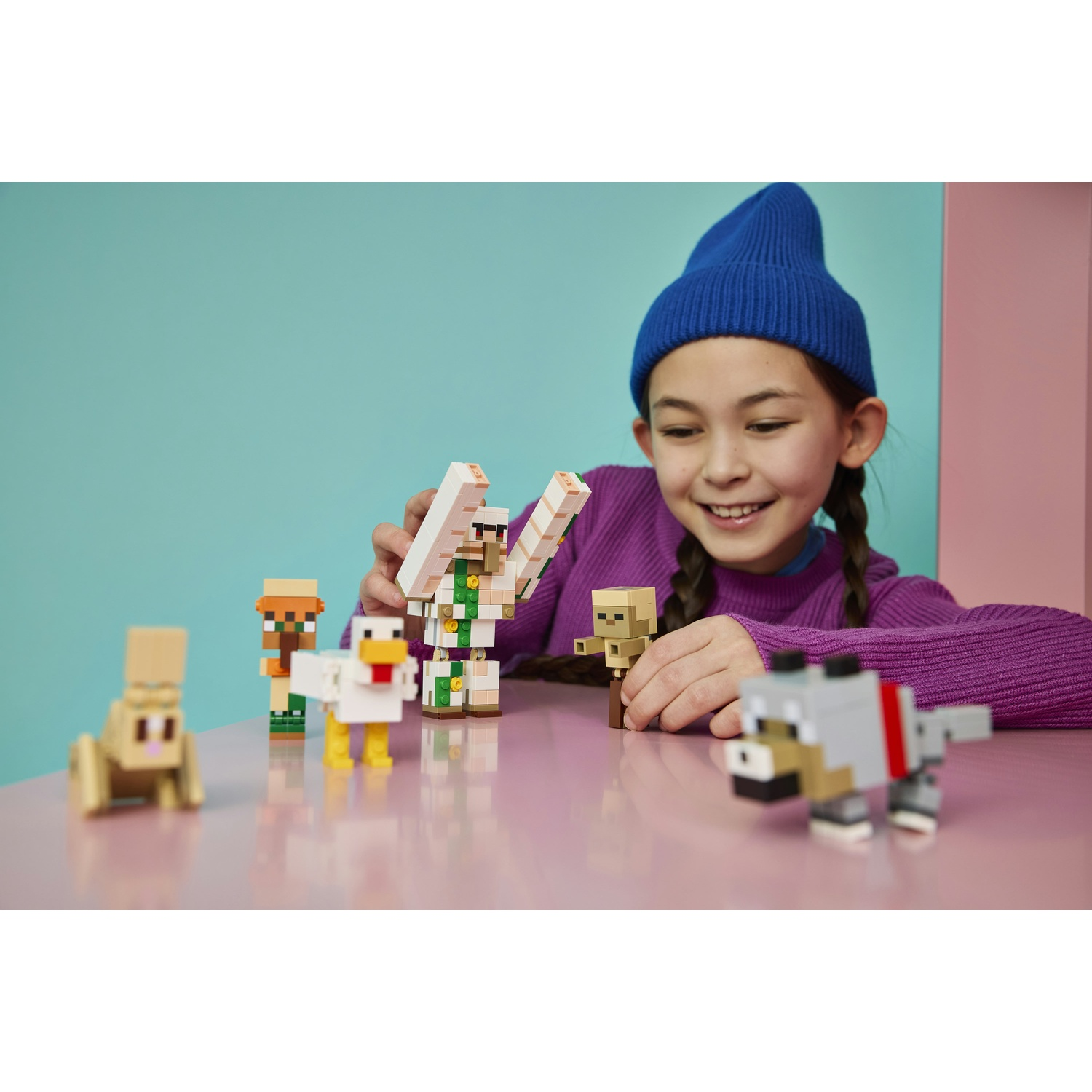 Bambina con cappello blu gioca con figure Minecraft: coniglio, pollo, abitante, lupo, golem.