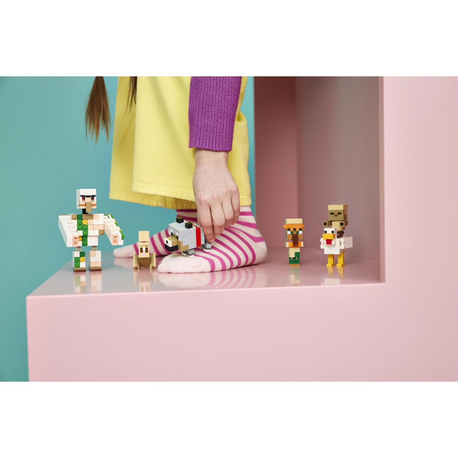 Un bambino con calzini a righe costruisce una minifigure accanto ad altre figure.