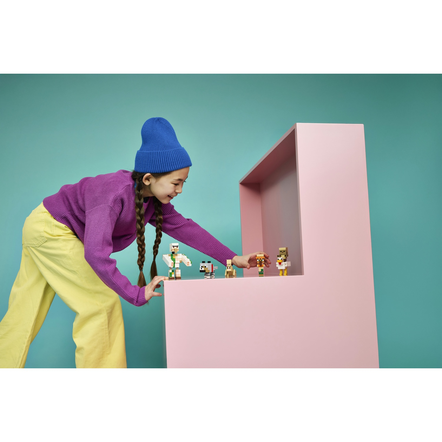 Una ragazza in maglione viola e pantaloni gialli gioca con piccole figure.
