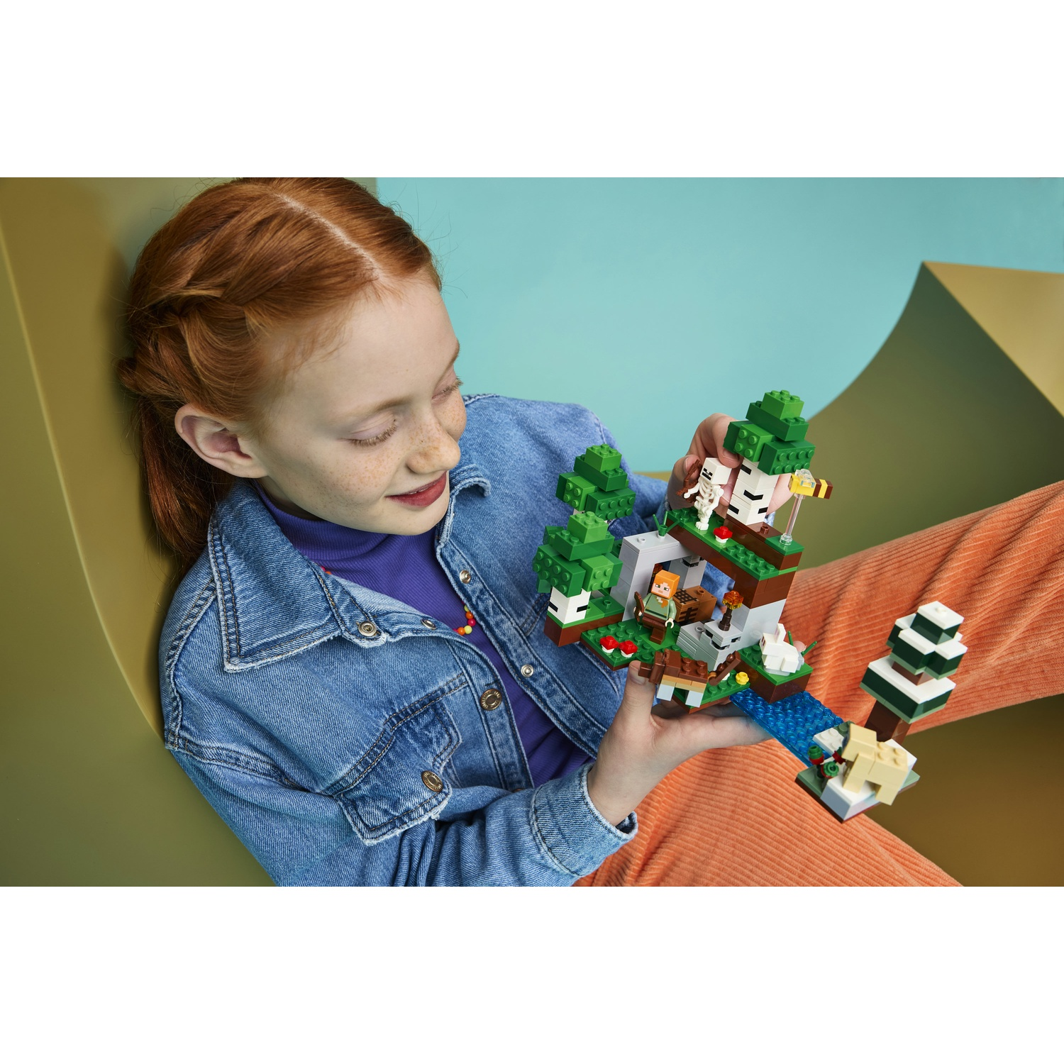 Una bambina dai capelli rossi tiene un set Lego Minecraft con alberi, animali e una figura.
