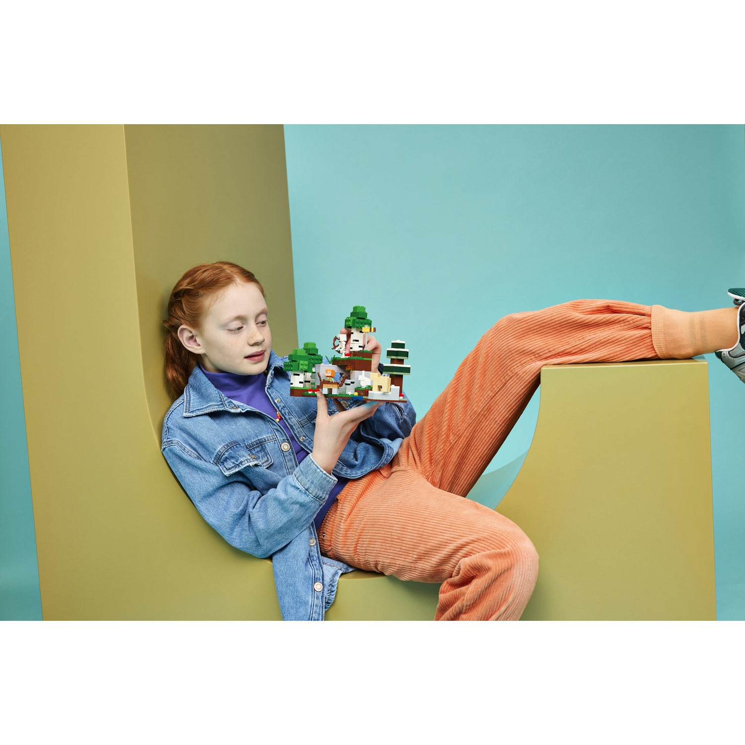 Bambina dai capelli rossi in giacca di jeans tiene una scena Lego Minecraft.