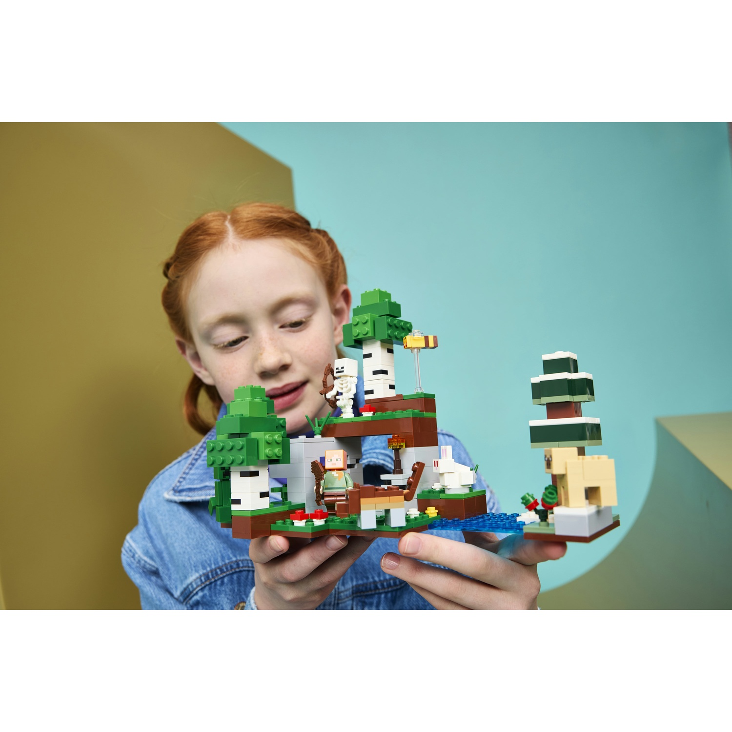 Una ragazza tiene un set Lego Minecraft con alberi, uno scheletro, un coniglio e un lama.