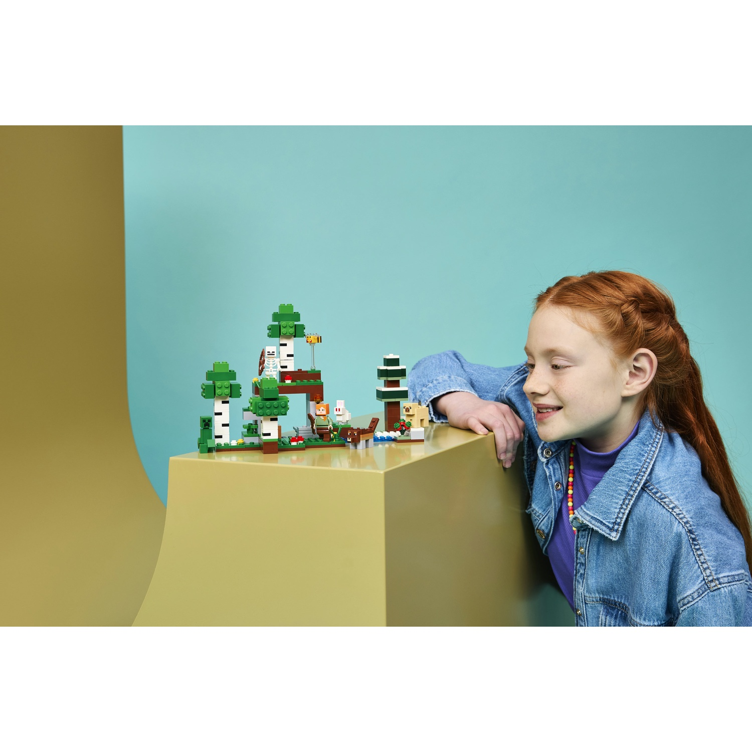 Bambina dai capelli rossi osserva un set Lego di Minecraft con alberi, uno scheletro e un coniglio.