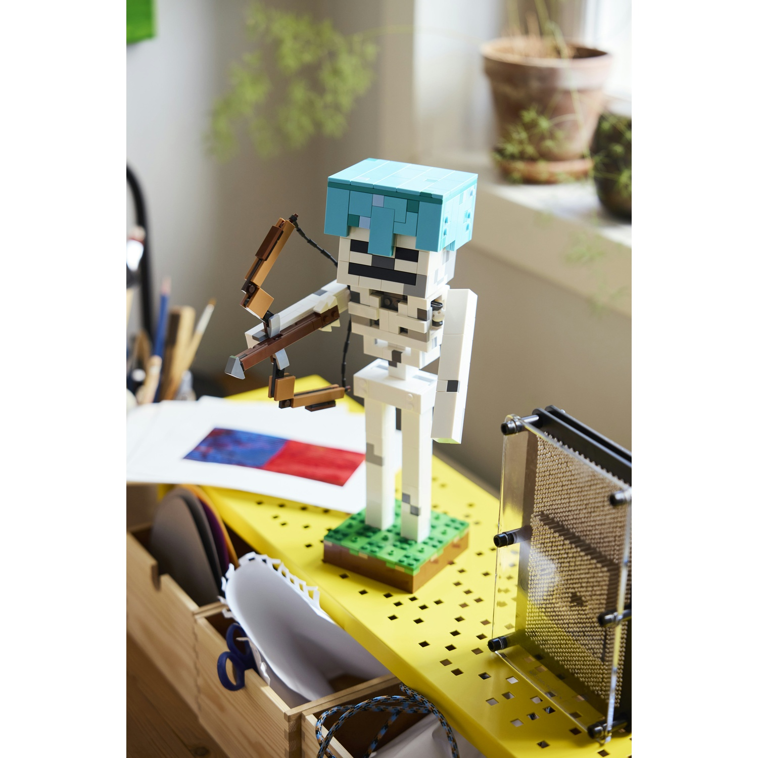 Una figura scheletrica Lego Minecraft con arco e casco blu sta su una base verde.