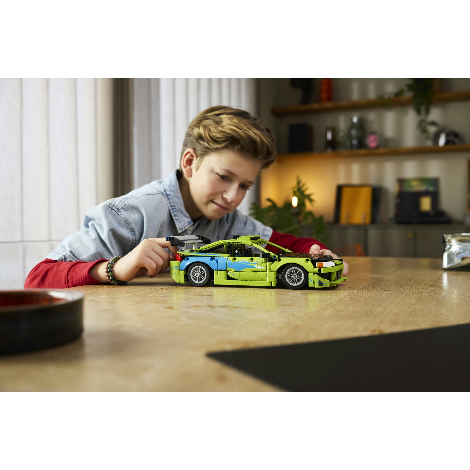 Un ragazzo costruisce un'auto sportiva Lego verde brillante con accenti blu.