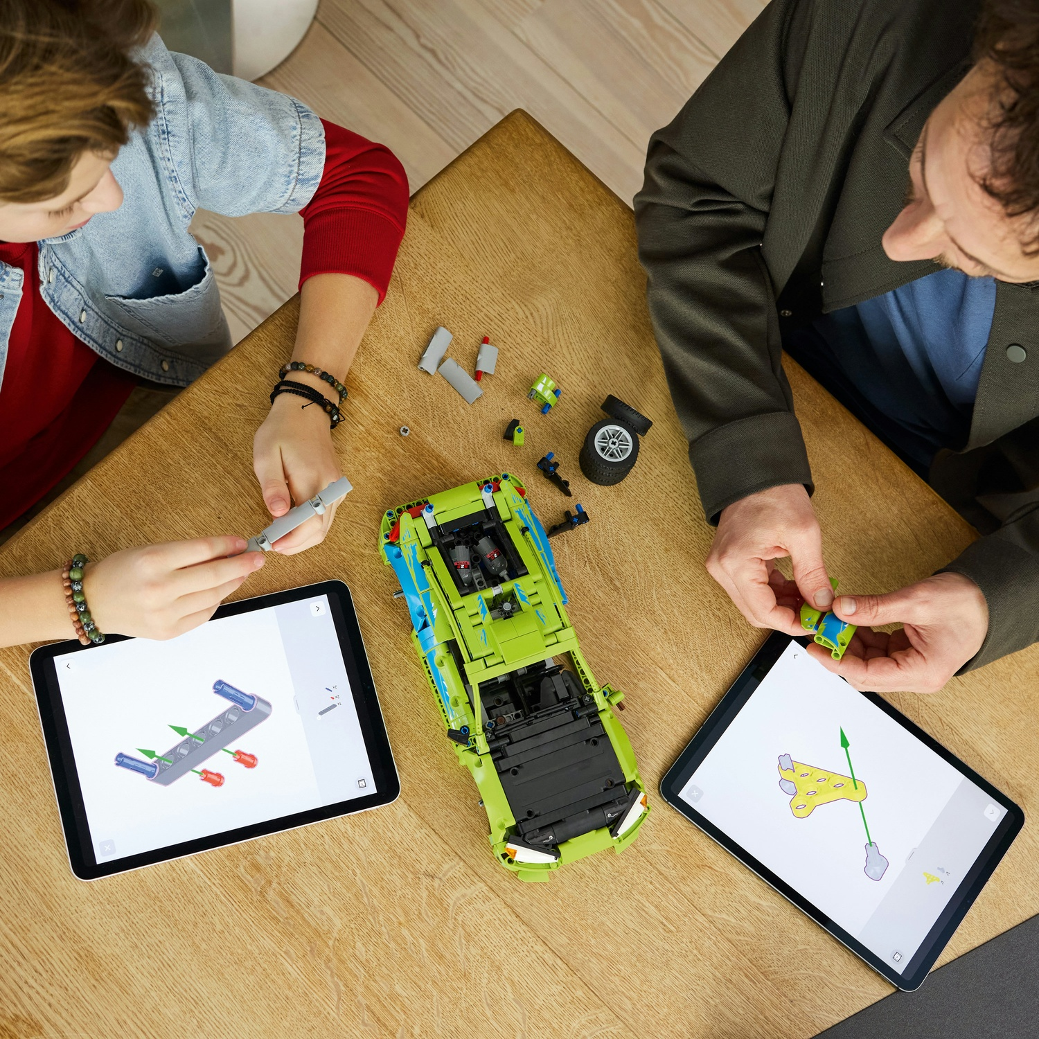 Due persone costruiscono un'auto Lego verde usando tablet con istruzioni.