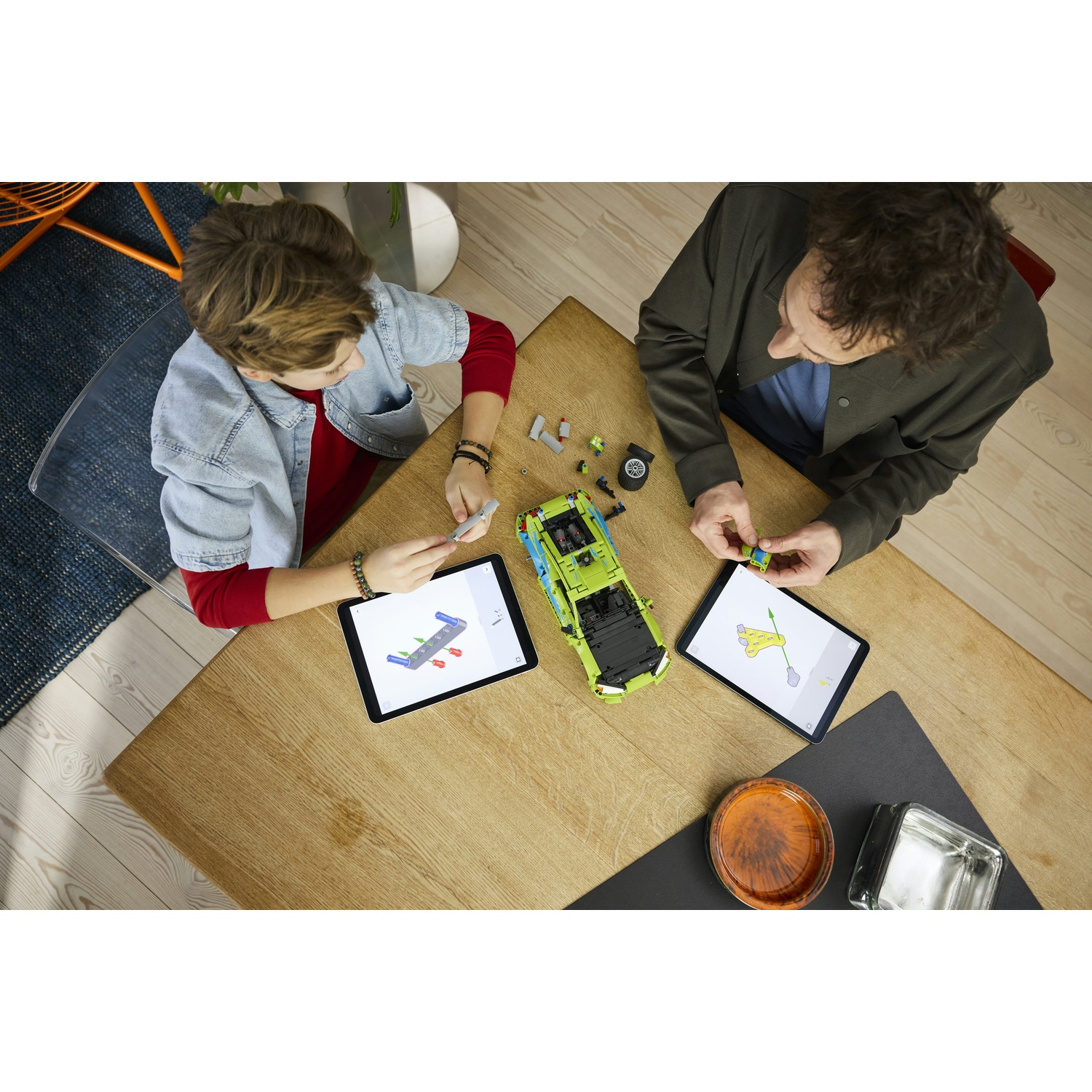 Uomo e ragazzo costruiscono auto con tablet su tavolo di legno.