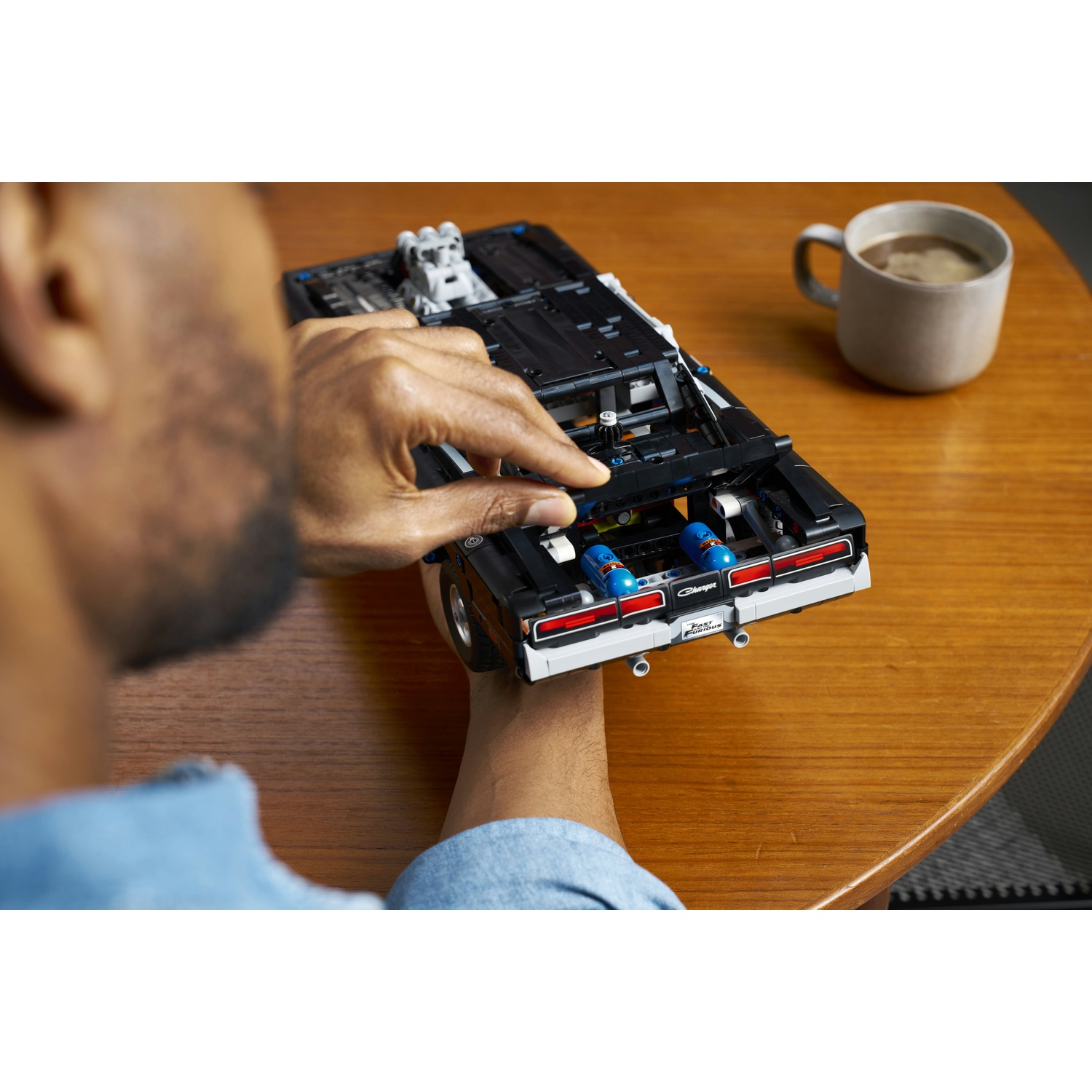 Una persona assembla una LEGO Dodge Charger nera con dettagli blu e una tazza di caffè.