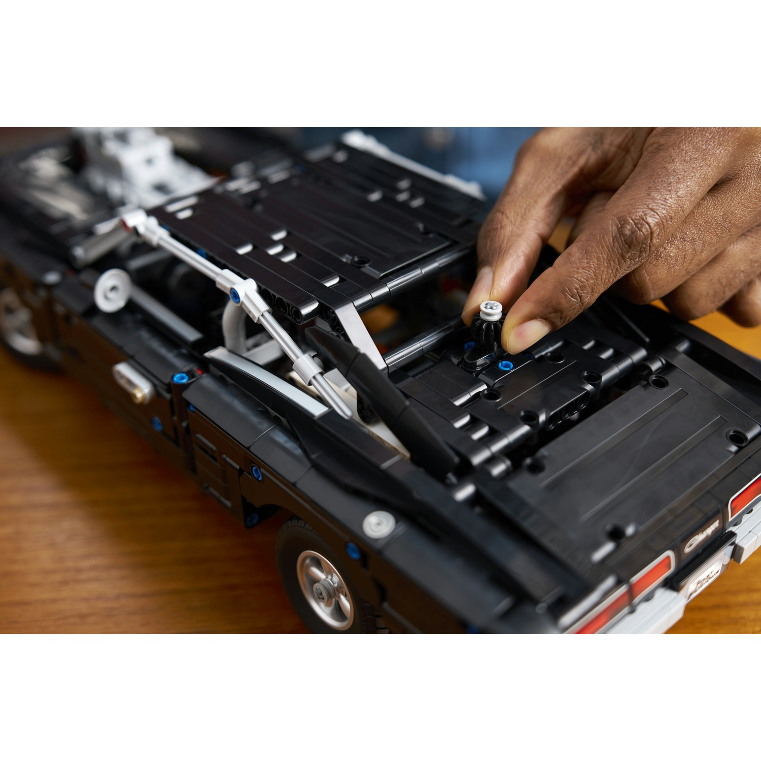 Persona che monta auto Lego nera, inserisce piccola parte.