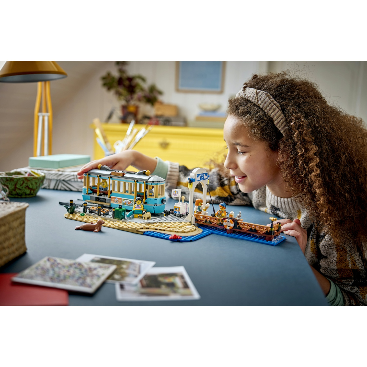 Una ragazza gioca con un set Lego con un tram e un molo.