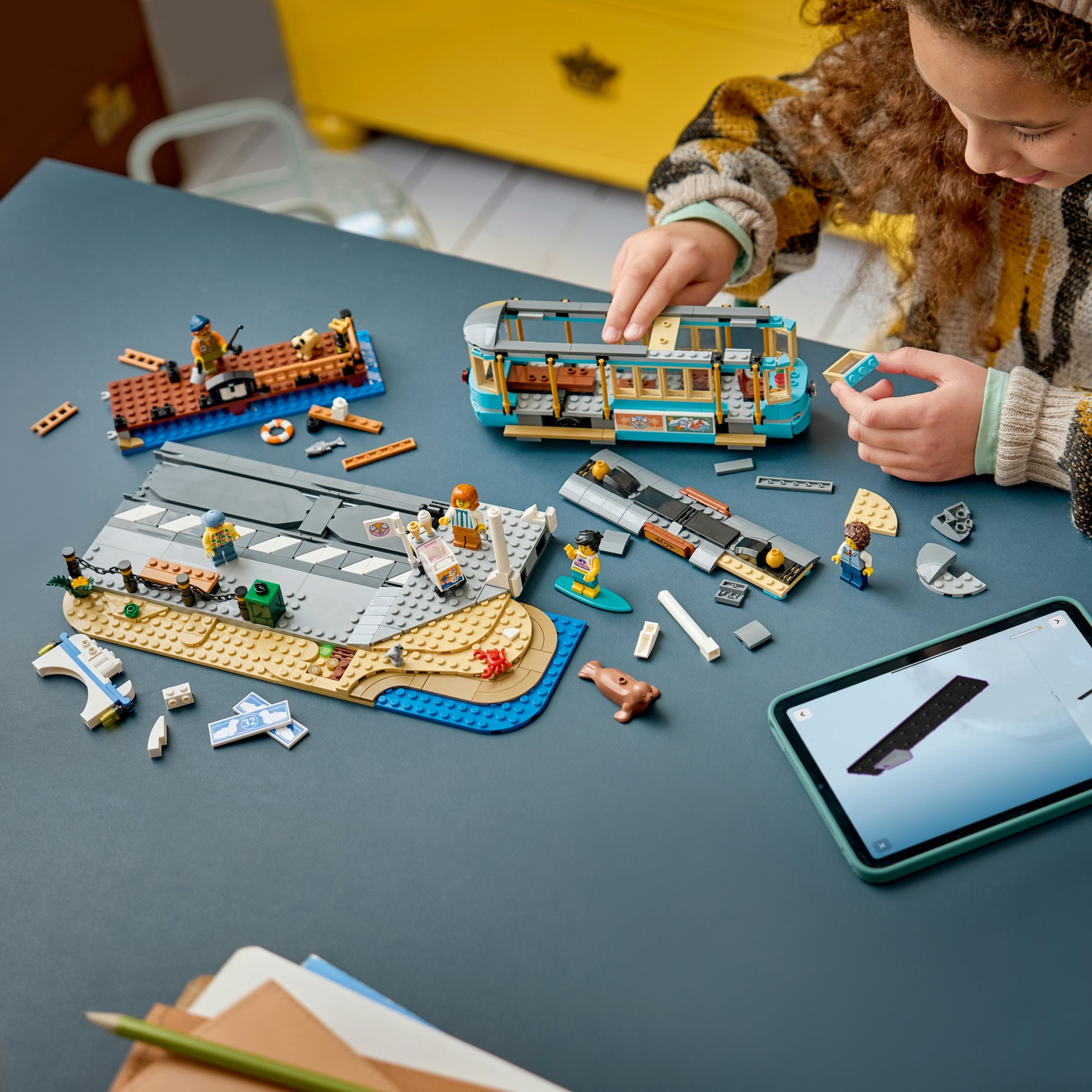 Una bambina costruisce set Lego su un tavolo, tra cui un tram e una barca.