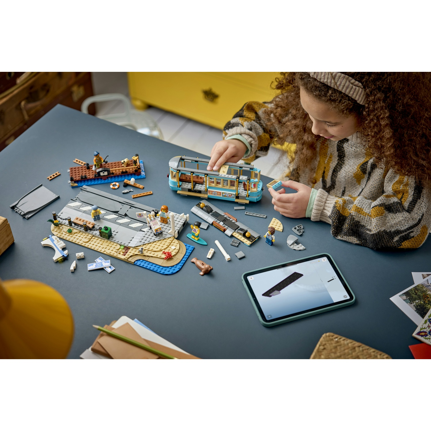 Una ragazza costruisce un tram Lego e altri modelli su un tavolo, con un tablet.