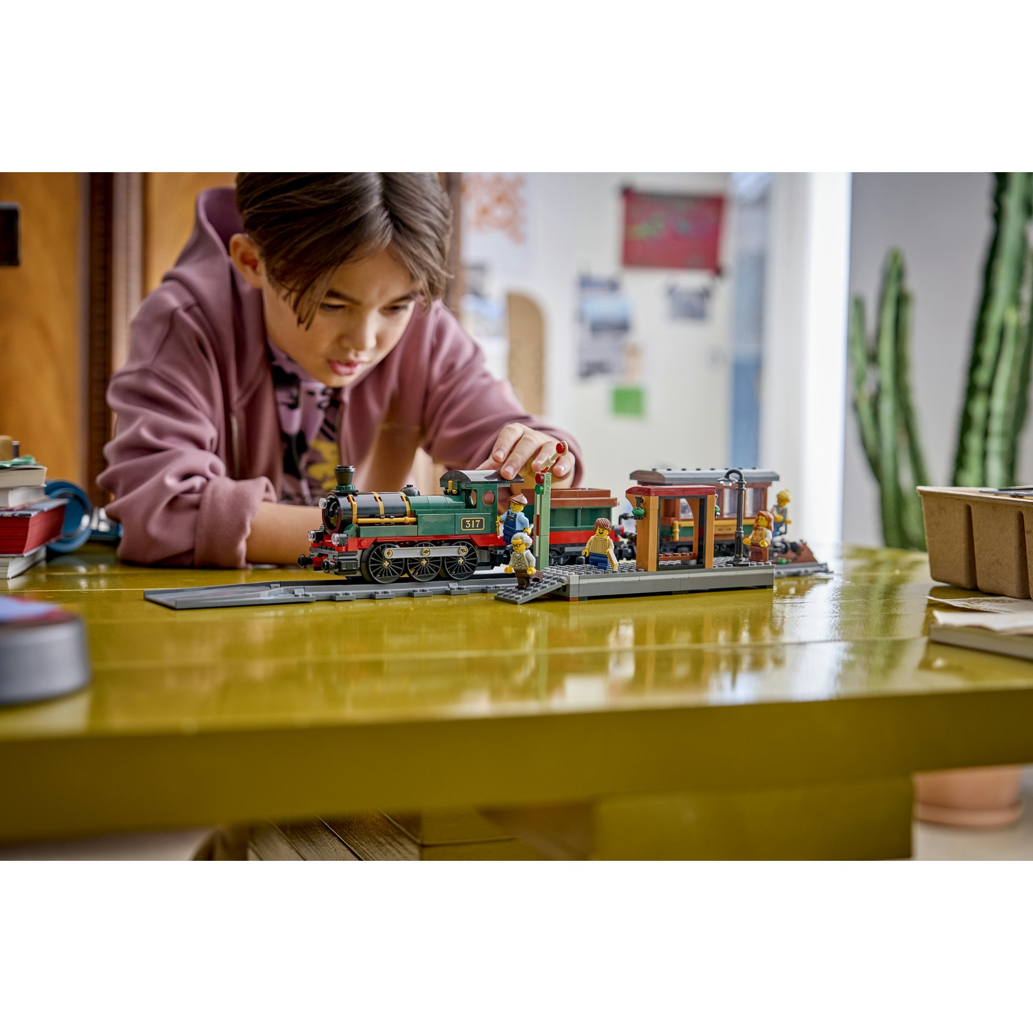 Un ragazzo gioca con un trenino Lego su un tavolo giallo. Treno verde con tre carrozze e figure.