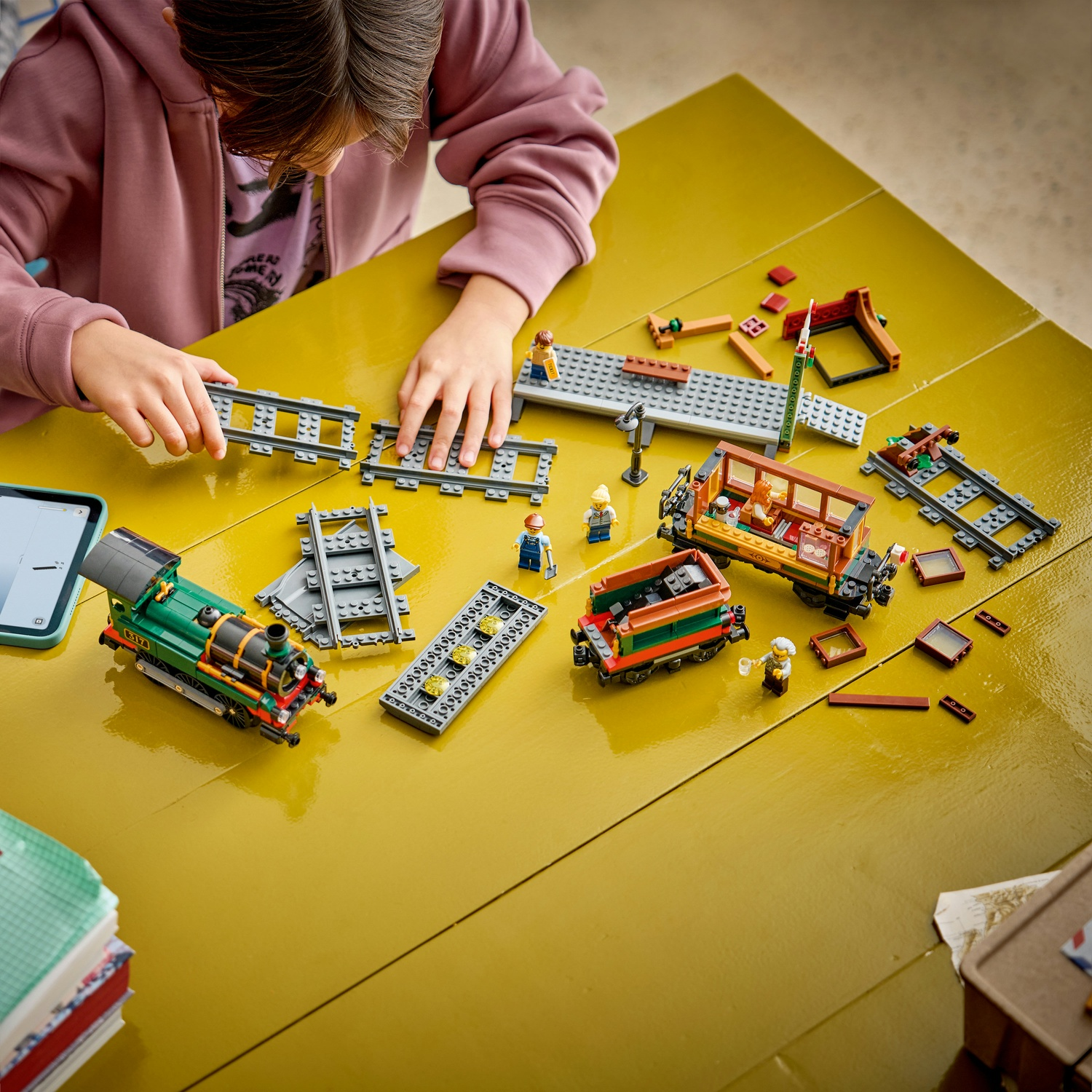 Bambino costruisce un set di treno Lego su tavolo giallo con vagoni verdi e arancioni.