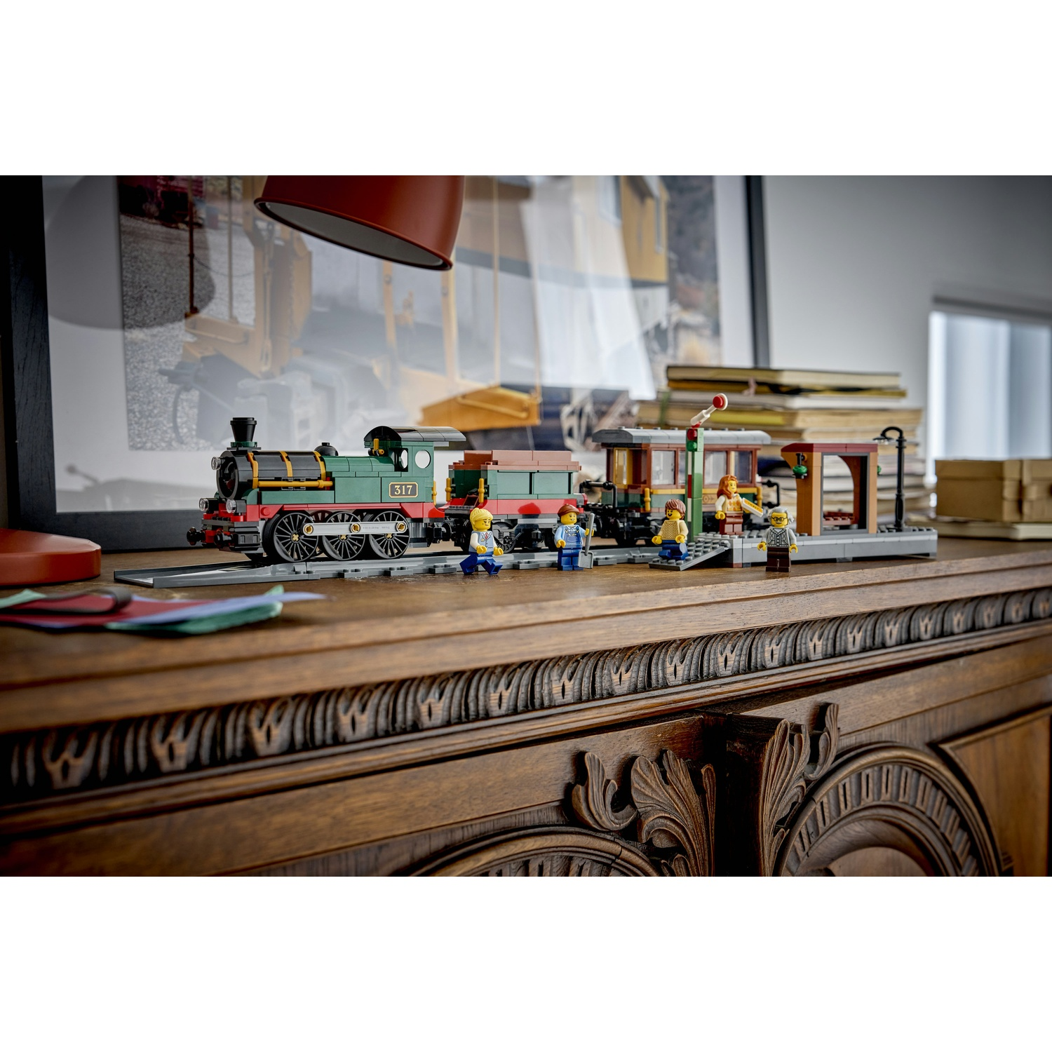 Un treno Lego verde con figure in una stazione su un comò di legno.