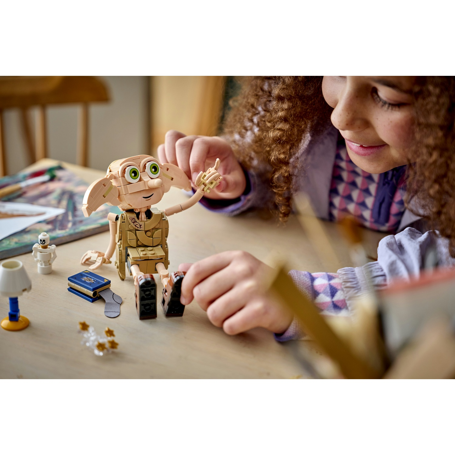 Una ragazza costruisce una figura di Dobby LEGO con libro, calzino e lampada.