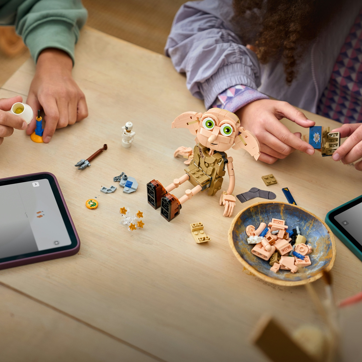I bambini costruiscono una figura Lego di Dobby attorno a un tavolo con tablet e pezzi.