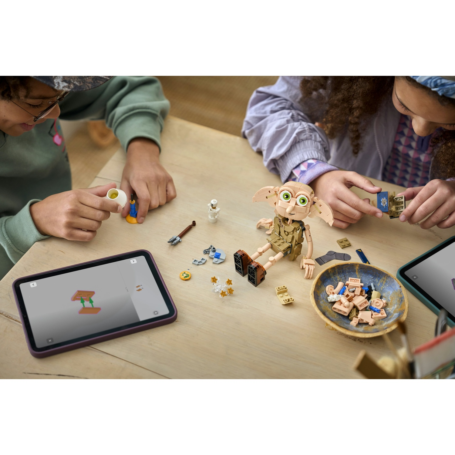 Due bambini costruiscono con Lego su un tavolo di legno. Un modello di Dobby è in primo piano.