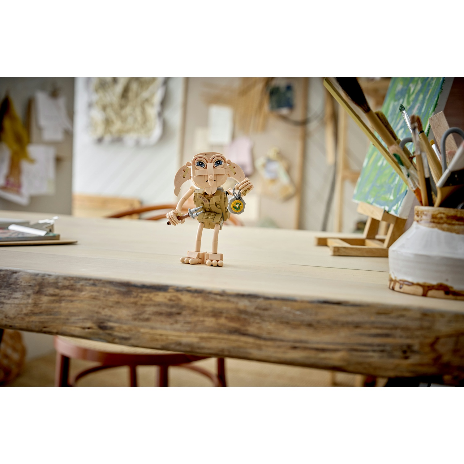 Una figura Lego di Dobby si trova su un tavolo di legno, tenendo un calzino. Forniture artistiche sono vicine.