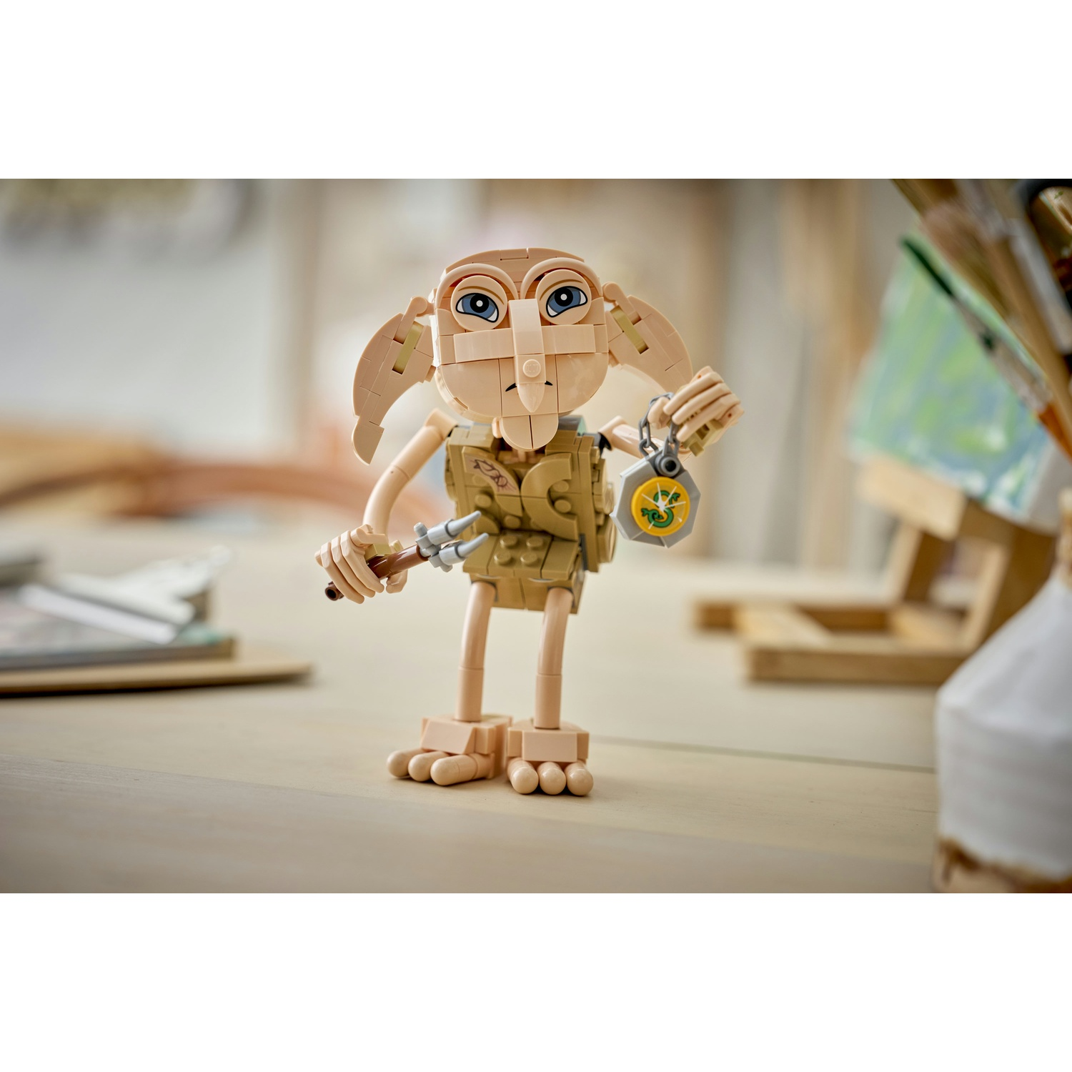 Una figura Lego di Dobby con medaglione e pugnale su un tavolo di legno.